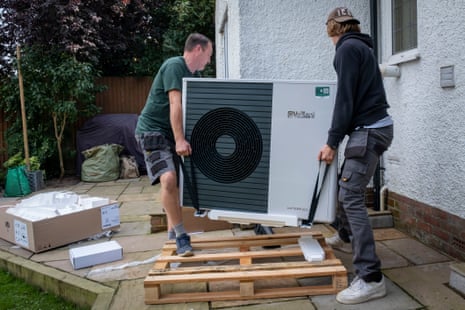 Installers carry an air source heat pump unit using straps, outdoors