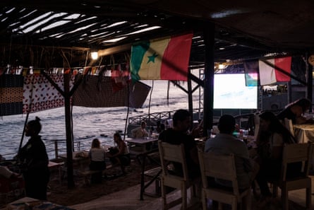 People sit at a restaurant on the coastline watching a world cup match on a large screen in Dakar.