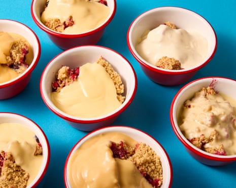 Red and white bowls of fruit crumble topped with custard, sitting on a blue surface