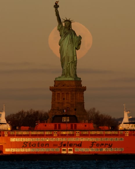 The moon sets behind the Statue of Liberty