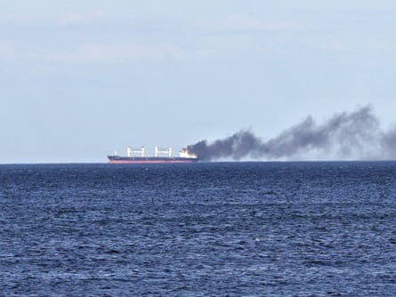 A ship on the horizon with black smoke rising from the rear of the vessel into the sky.