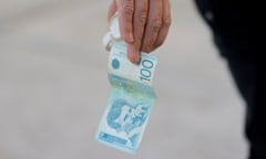Close-up of a hand holding a 100-dinar note.