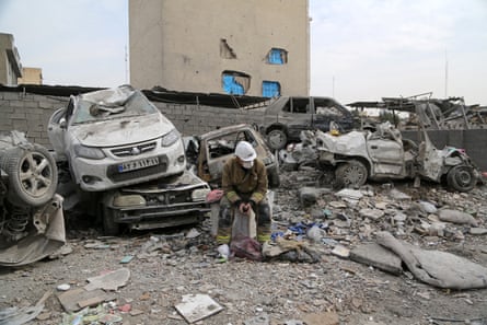 A search and rescue member sits in the rubble of a damaged building with cars stacked on top of each other