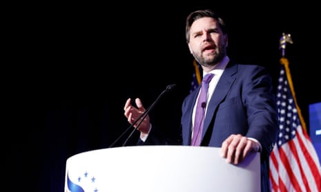 man in a suit speaks at a lectern with an american flag behind him