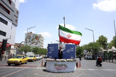 A woman holds Iran's national flag as she stands behind a wall that stands in the middle of a street in between the lanes of traffic