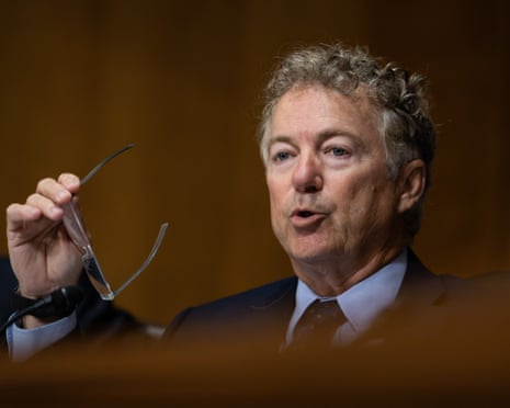 man in suit holds glasses while speaking