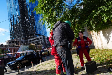 First aiders provide medical attention as damaged buildings can be seen in the background.