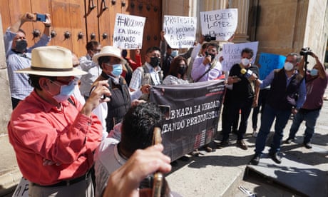 Men and women stand in a plaza holding signs in protest of the attacks on journalists.