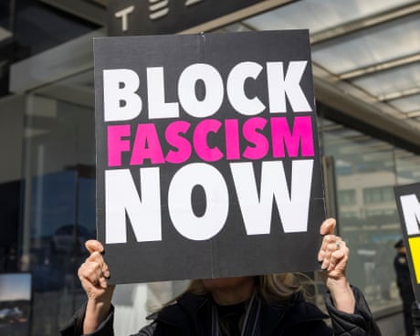 a person holds a sign that reads 'block fascism now'