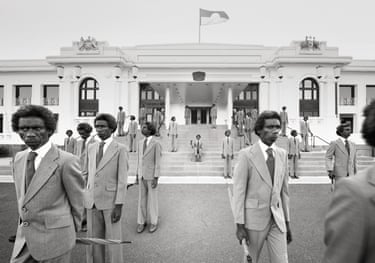 Majority Rule (parliament) 2014. A monochrome image of an Indigenous man in a grey suit in various poses outside a parliamentary-style building. The Aboriginal flag is flying from the roof of the building.