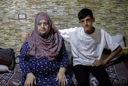 A teenaged Arab boy in a T-shirt and jeans sits with his arm around an older woman in a headscarf