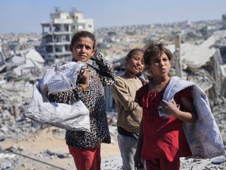 Children hold sacks amid rubble of destroyed buildings.