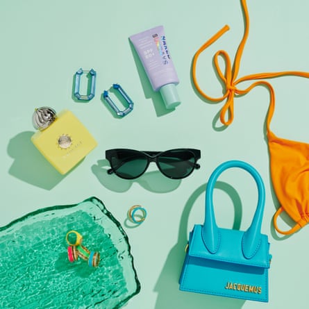 Black sunglasses in the centre. Perfume, earrings, sun lotion, orange bikini, blue handbag and colourful rings scattered around it.