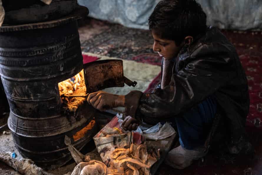 A boy feeds scraps of plastic into a fire