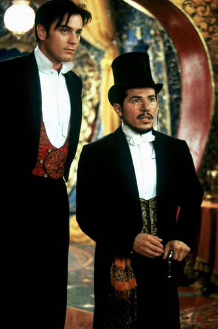 Two men, both wearing black suits, white shirts and waistcoats, standing in front of a curved red and gold arch
