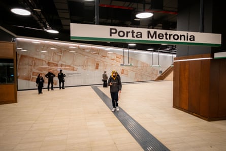 People walking in station with Porta Metronia sign above and some looking at information board about finds behind