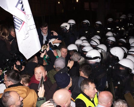 A crowd and press face riot police outside Poland’s Constitutional Tribunal at night