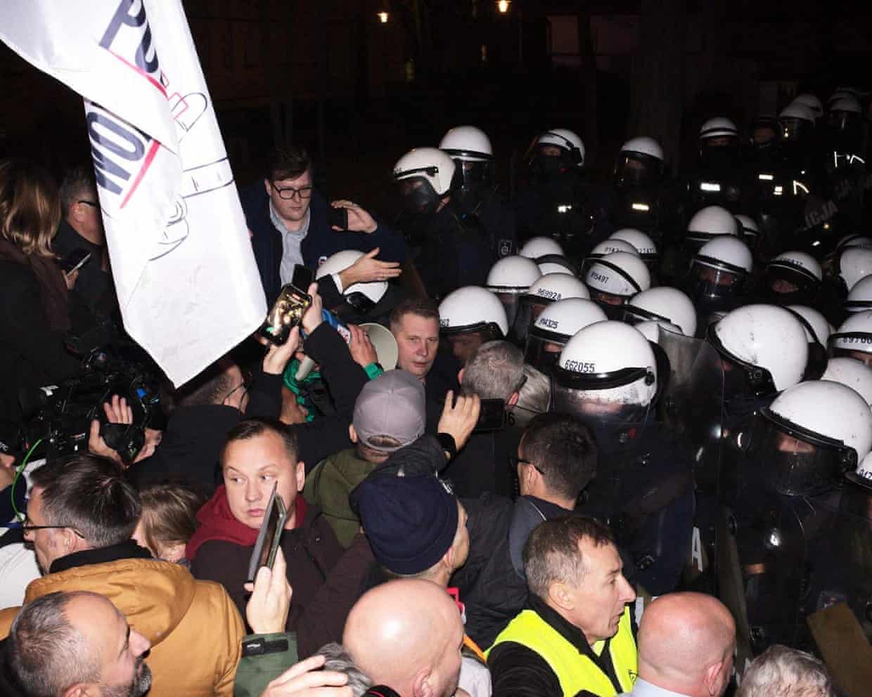 A crowd and press face riot police outside Poland’s Constitutional Tribunal at night