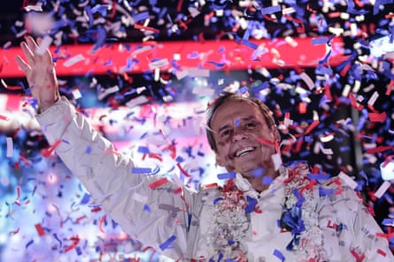 a man in a white shirt waves amid coloured confetti