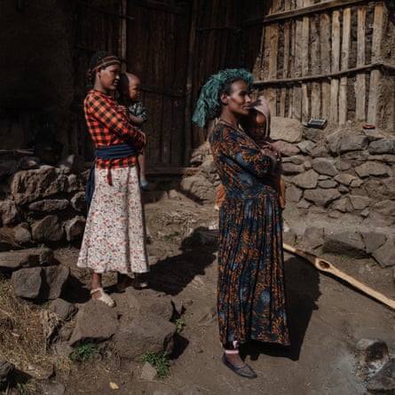 Two women stand next to stone and log building