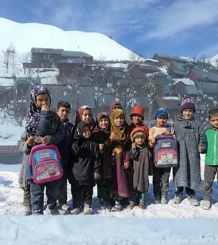 A group of young children, some carrying backpacks, smile as they stand together on snowy ground