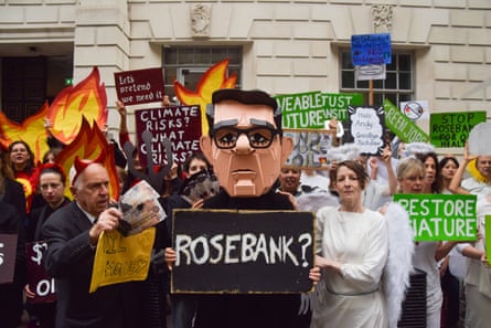 A protester in a Burnham mask holds a “Rosebank?” sign amid activists dressed as devils and angels