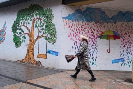 Woman walks past decorated building site hoarding in Warrington