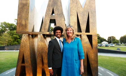 Standing in front of a nearly two-story-high gold sculpture of letters that spell ‘I Am a Man’ are a young Black man with glasses and a dark suit on the left, and a middle-aged  white woman with long blond hair and a long blue linen shift dress.