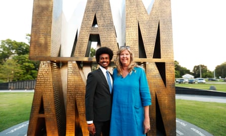 Standing in front of a nearly two-story-high gold sculpture of letters that spell ‘I Am a Man’ are a young Black man with an Afro and glasses and a dark suit on the left, and a middle-aged woman with long blond hair and a long blue linen shift dress.