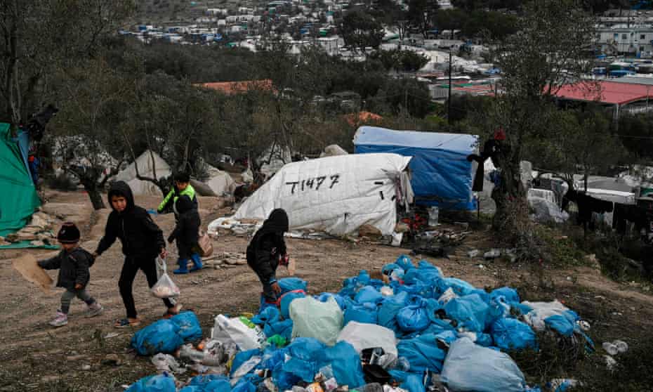 Children walk next to bags of refuse at a makeshift camp next to the Moria refugee camp in Lesbos