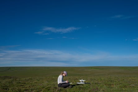 A woman in a cap sits working on the grass next to a drone