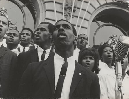 Men in suits and women in gowns sing into a microphone