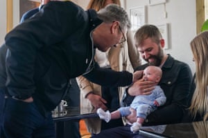 A man holds a baby who looks at Keir Starmer at he bends down in front of them