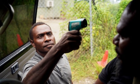 A guard from a logging mill in East New Britain province in Papua New Guinea, checks the temperature of police and passengers in the vehicle before they are allowed to enter the compound.