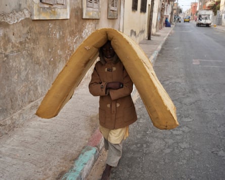 A young boy walks along a road with a foam mattress balanced on his head