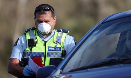 A masked police officer stands next to a car with papers in his hand