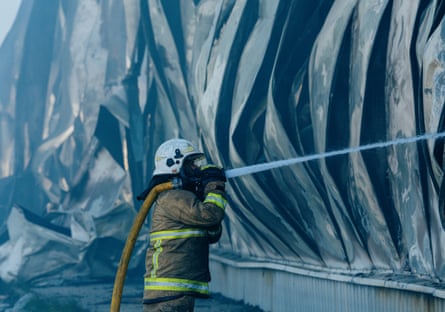 A firefighter sprays water on the warehouse after the Russian attack in Kyiv region