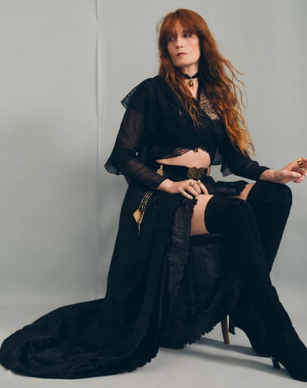 Florence Welch sitting on a chair, wearing a flowing black outfit and long, black boots