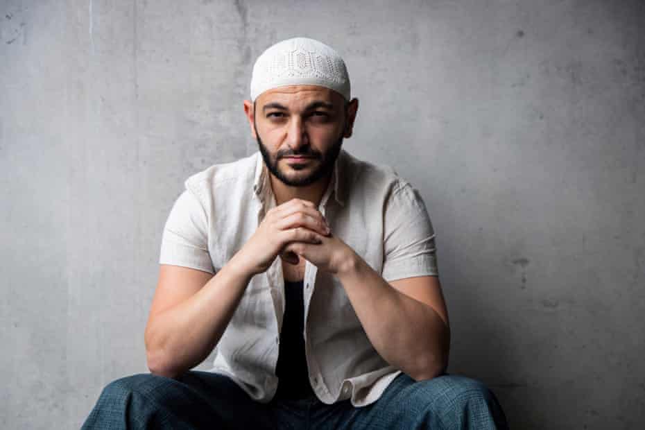 Arab-Australian author Michael Mohammed Ahmad rests elbows on his knees and looks at the camera