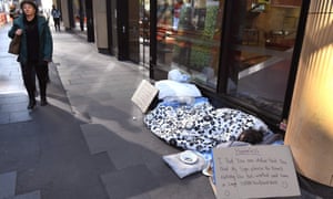 A homeless man lies on the ground in front of a store begging for money in Sydney’s CBD.