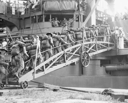 A black and white photo of marines with supplies on their backs crossing a gangplank on to the USS Connecticut