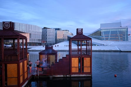 People in swimwear standing by a floating sauna.