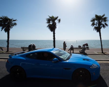 People sit on benches looking over the beach as a Jaguar XKR-S passes on the promenade in Southend, England.