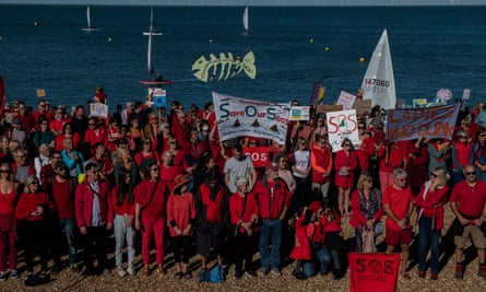 Dozens of people gathered together on the beach in red tops holding protest banners