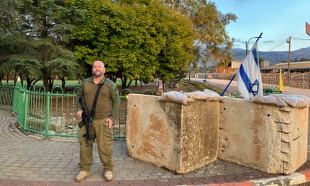 Lior Shelef looking at the camera while holding a gun and standing at a security post