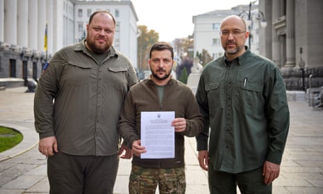 Volodymyr Zelenskiy holds up a copy of a request for fast-track membership of Nato, accompanied by Ruslan Stefanchuk (lef) and Denys Shmyhal, in Kyiv.