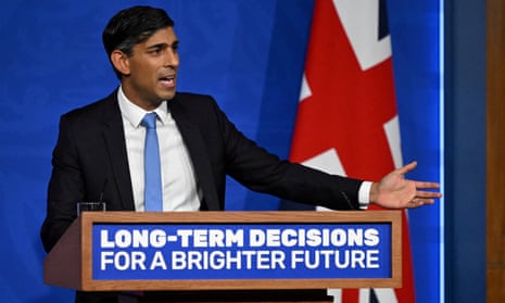 Rishi Sunak stands at a lectern bearing the words "Long-term decisions for a brighter future". He is delivering a speech and a Union Jack is visible behind him.