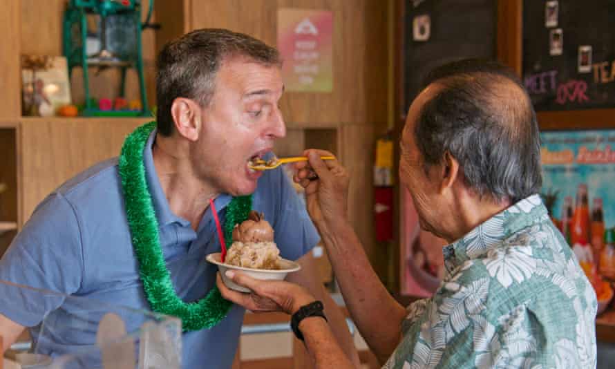 Phil Rosenthal is spoon-fed ice-cream while wearing a lei in Hawaii