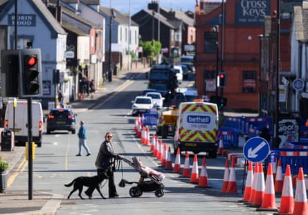 A person pushing a pram and leading a dog crosses the road with the high street in the background.