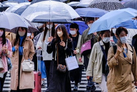 People wear face masks while walking through the intersection of Shinjuku, Tokyo.